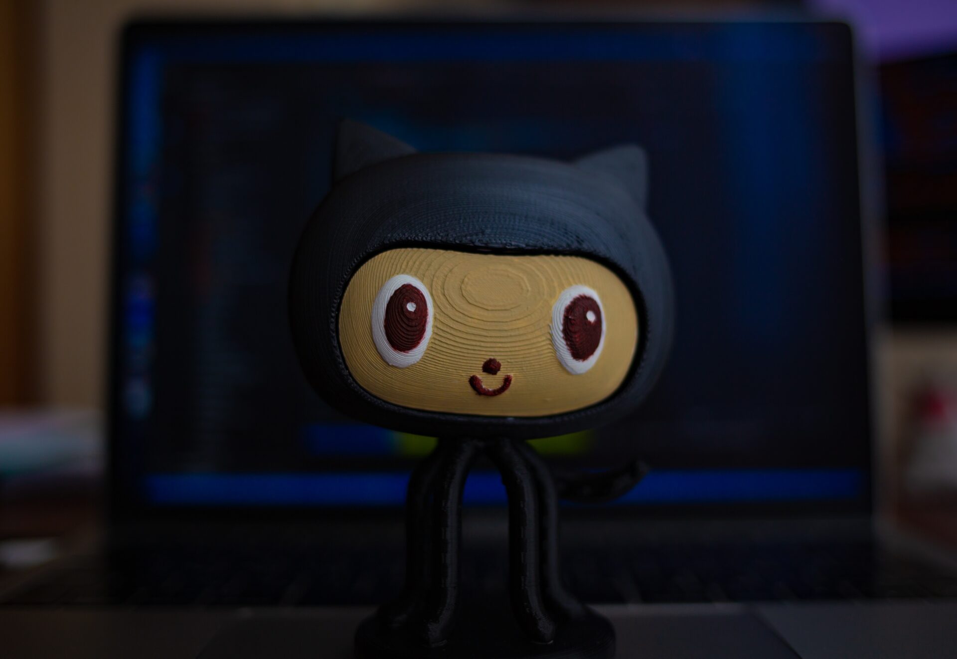 A small figurine of an oktokata in the center, in the background a laptop with an open code editor and a terminal.
